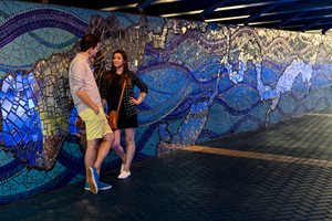 Photo of Two People standing next to the mosaic mural (Mirrored River: Where Do You See Yourself?) underneath the Main Street Bridge